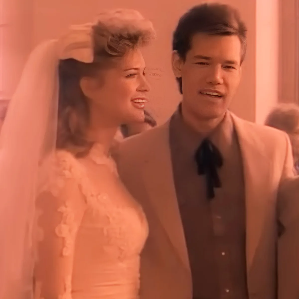A bride in a white dress and veil stands next to a man in a suit with a black bow tie.
