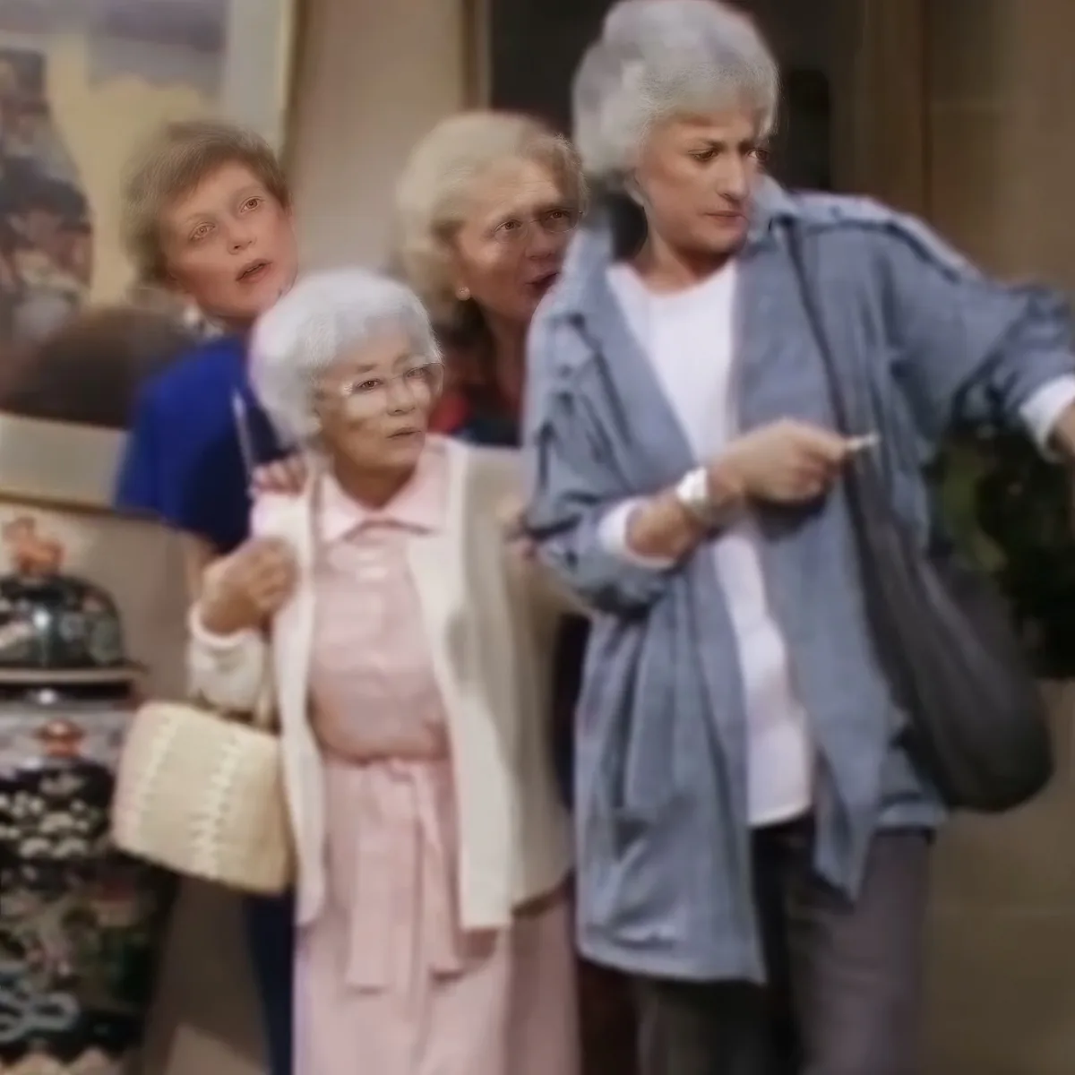 A woman in a blue shirt and gray pants points while holding a bag, with three other women in the background.