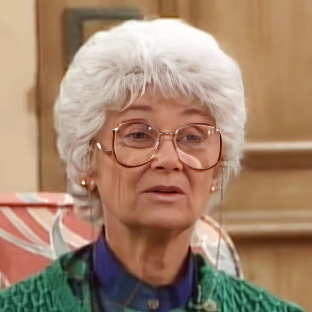 An elderly woman with white hair and glasses, wearing a green sweater, is looking to the side.