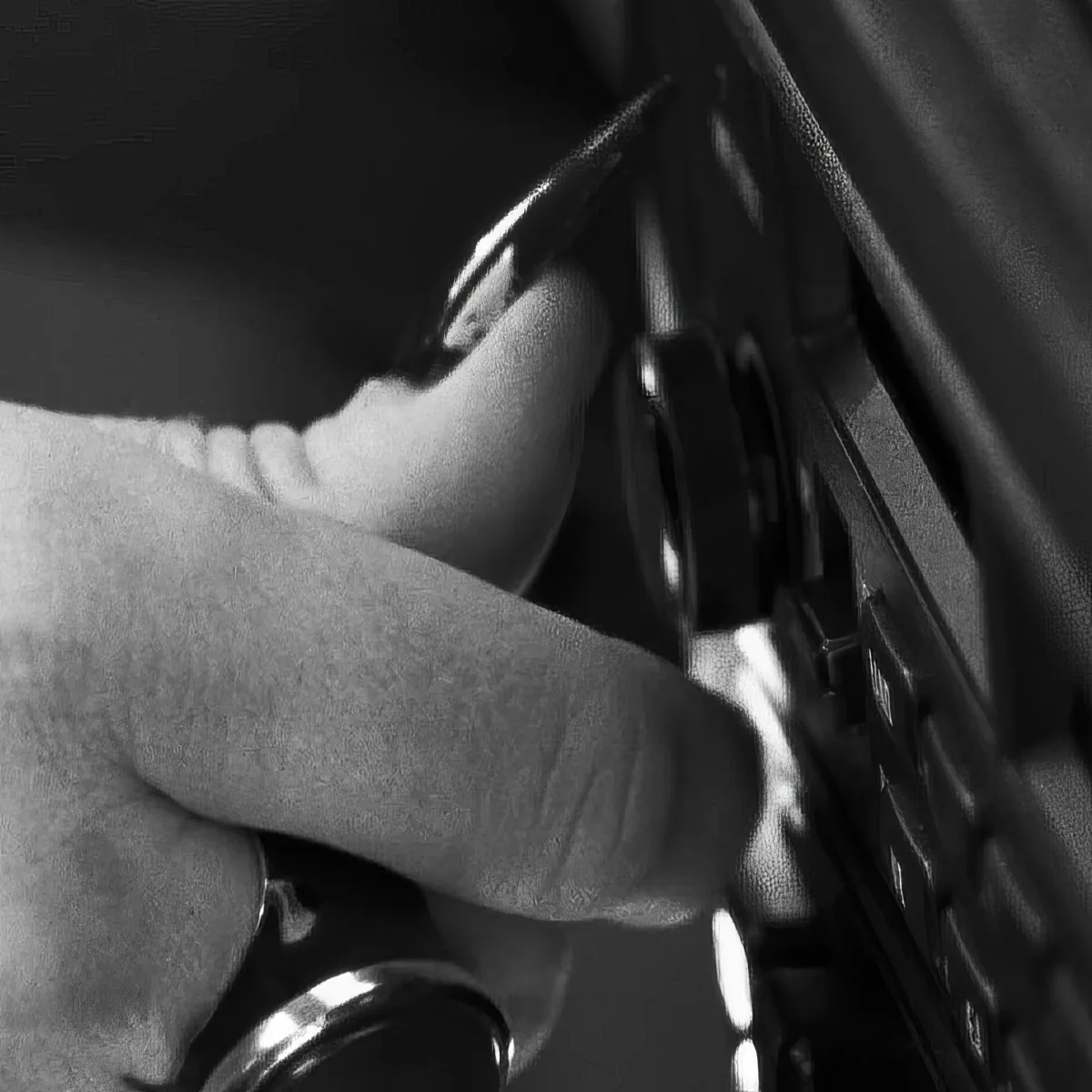 A hand is pressing a button on a dark, textured surface, possibly a vehicle's door handle.