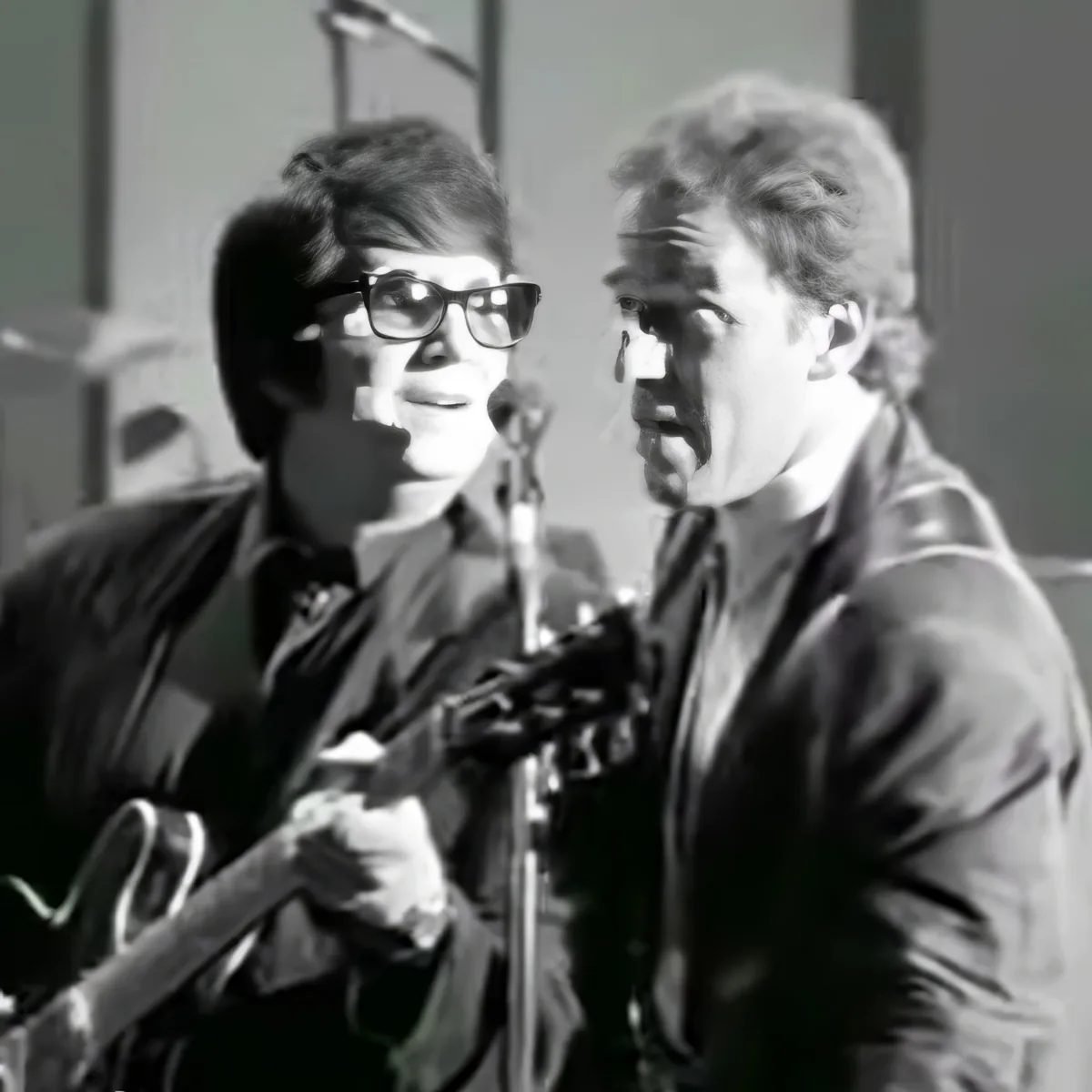 Two individuals, one playing guitar and the other singing, are captured in a black-and-white image.