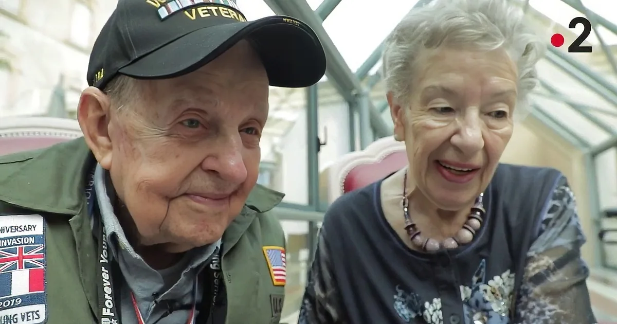 An elderly couple, the man in a World War II cap, tenderly holds each other in a car.