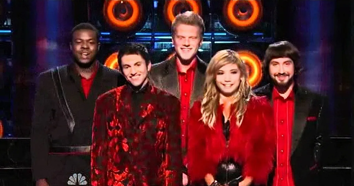 A group of five people, dressed in red and black, stand together on a stage with a colorful background.