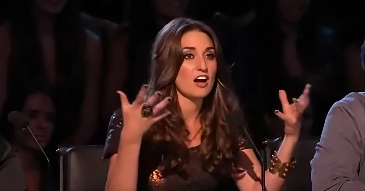 A woman with long brown hair gestures passionately with her hands while speaking.