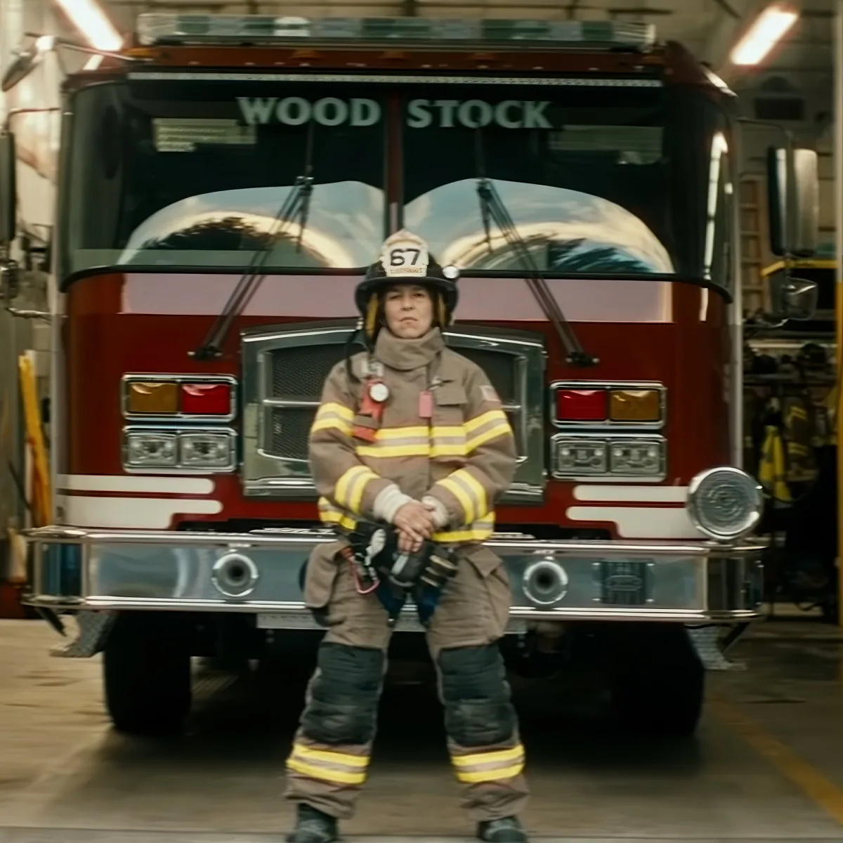 A firefighter in full gear stands in front of a red fire truck labeled "Woodstock."
