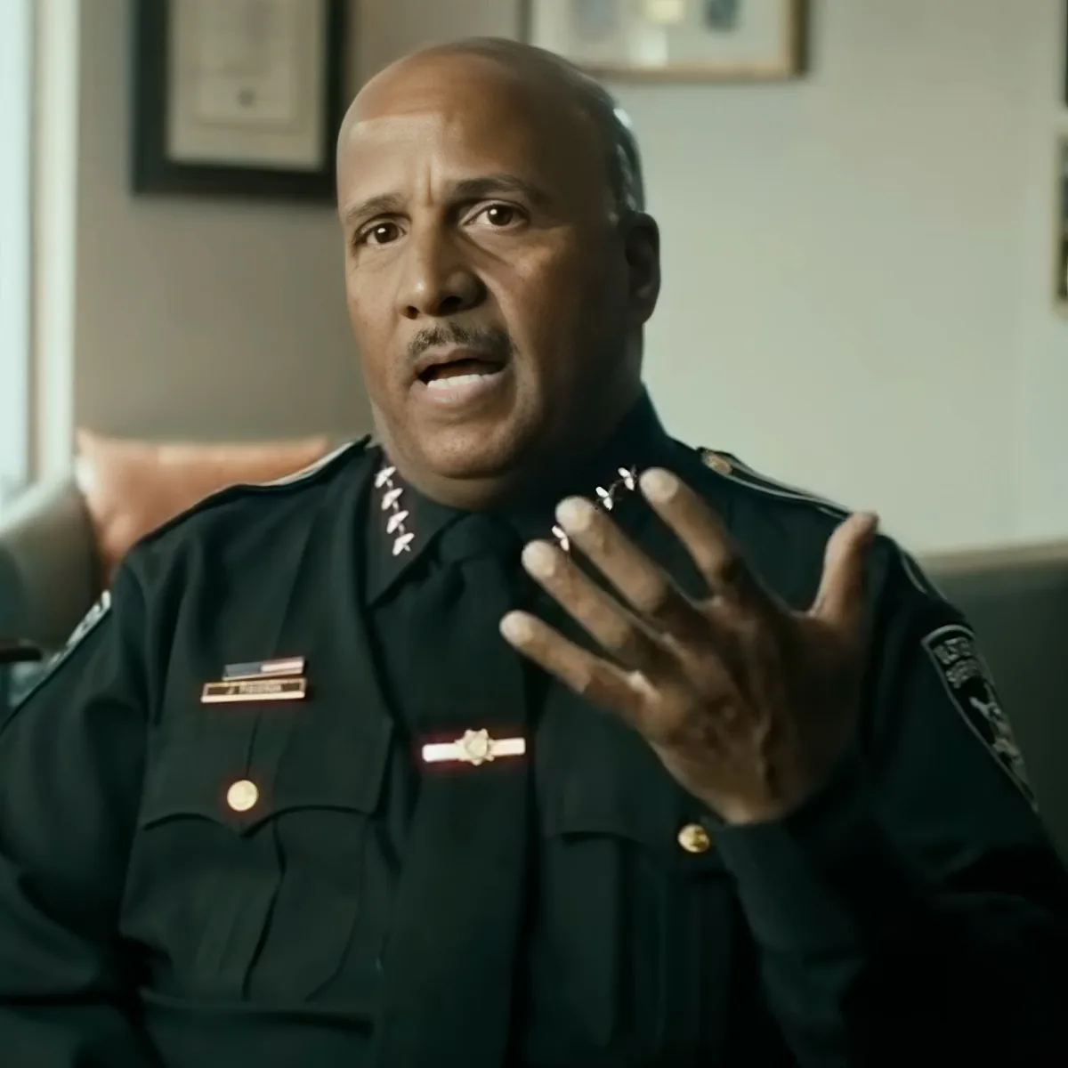 A man in a police uniform is speaking, gesturing with his right hand, and wearing a ring.