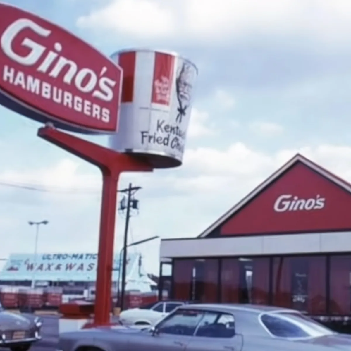 Gino's Hamburgers sign with a bucket of KFC chicken and a red building in the background.
