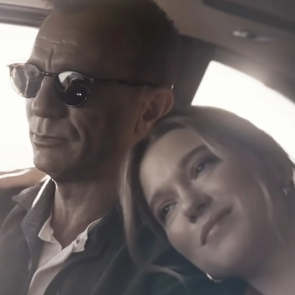 A man wearing sunglasses and a woman with long hair are sitting together in a car.