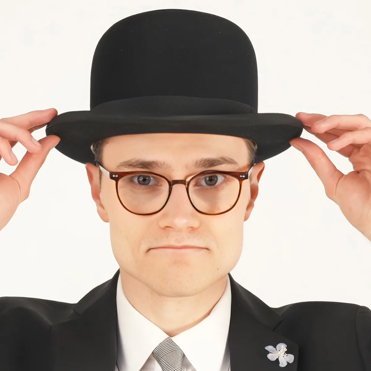 A person wearing a black suit, white shirt, tie, and round glasses adjusts a black top hat.