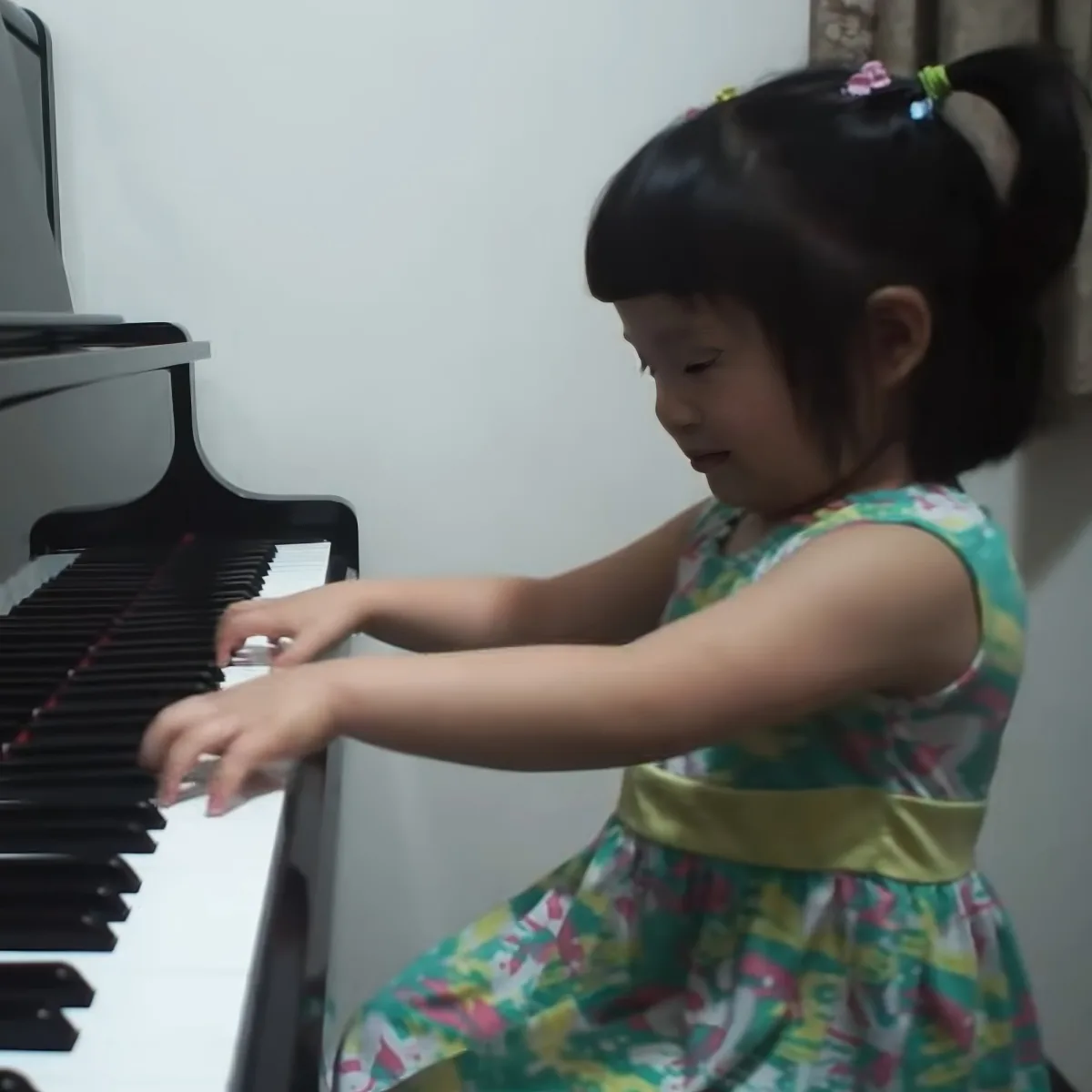 A young girl in a colorful dress plays a piano, her hands positioned on the keys.