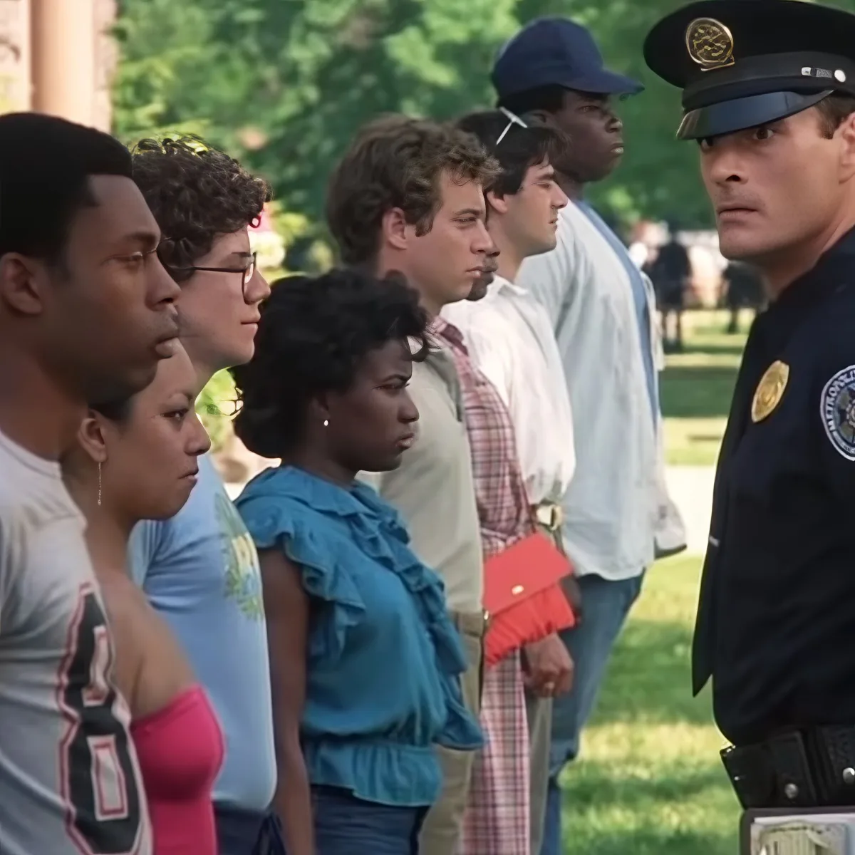 A police officer stands in front of a group of people, including a man in a plaid shirt and a woman in a blue blouse, in...