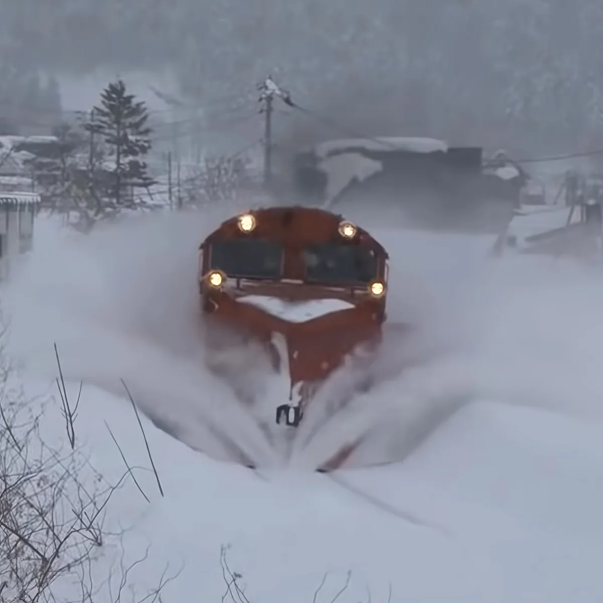 A red bus plows through deep snow, creating a dramatic wake behind it.