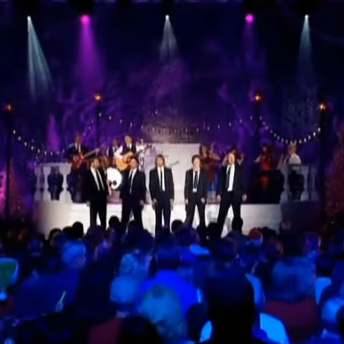 A group of men in suits stands on stage under colorful lights, surrounded by musicians and an audience.