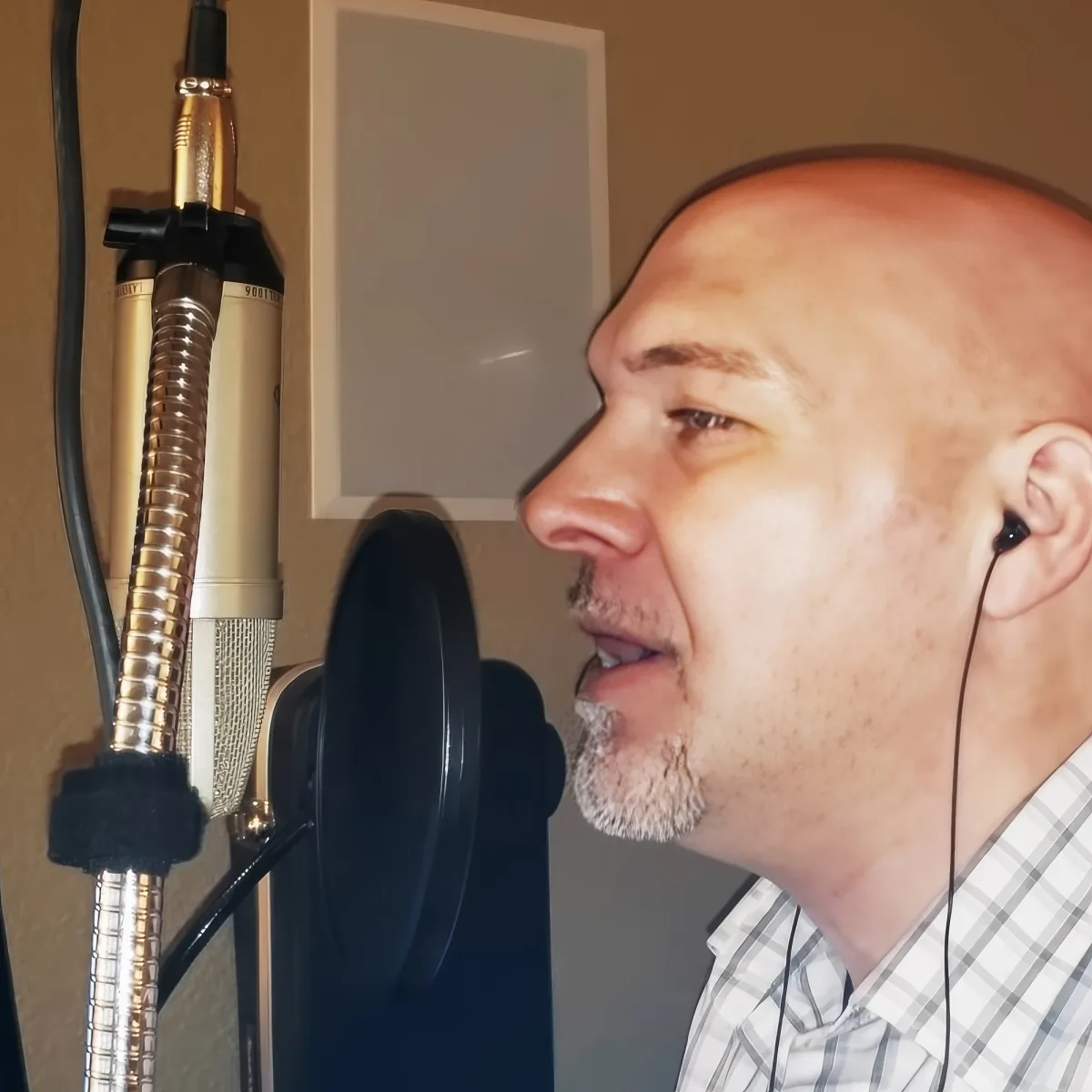 A man with a bald head and a goatee is singing into a microphone in a recording studio.