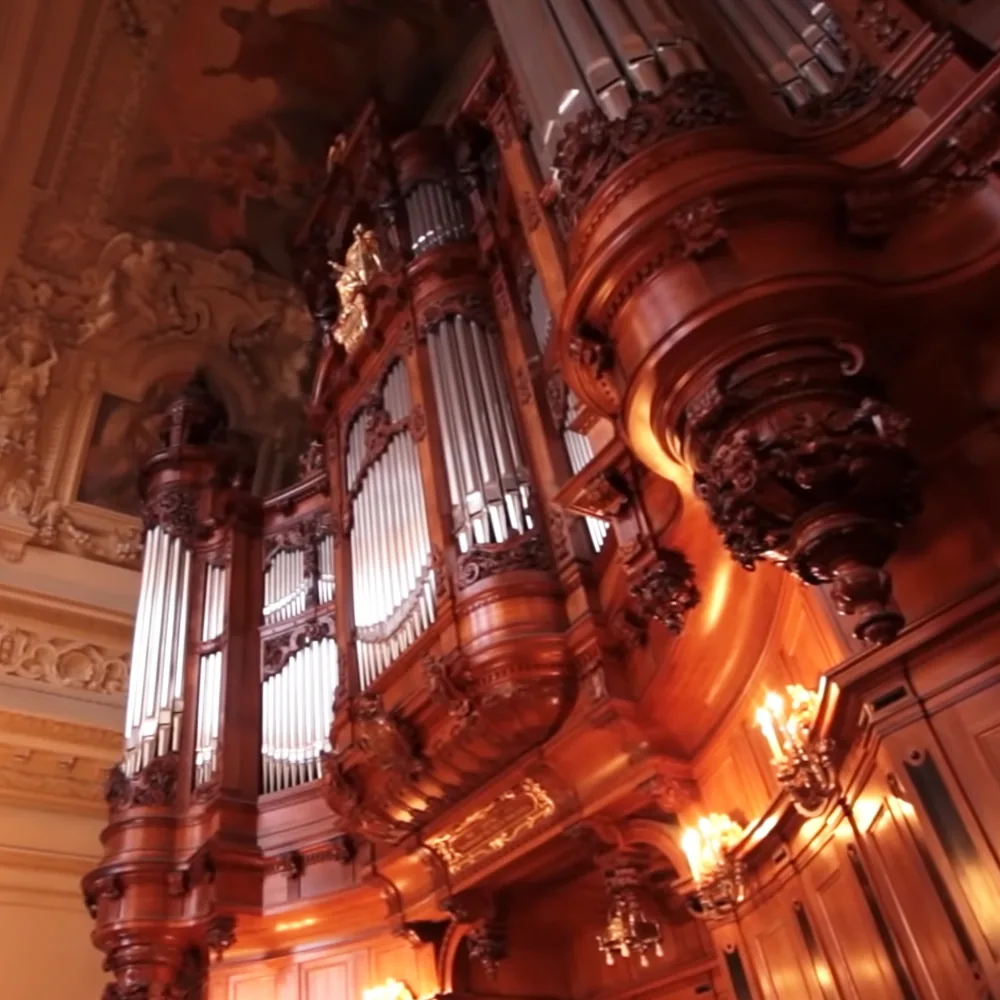 A grand, ornate pipe organ with intricate wood carvings and chandeliers is displayed in a luxurious setting.