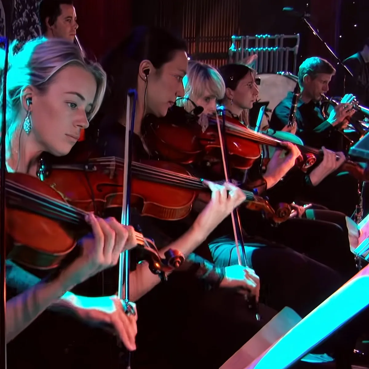 A group of musicians, including violinists, are performing on stage under vibrant blue lighting.
