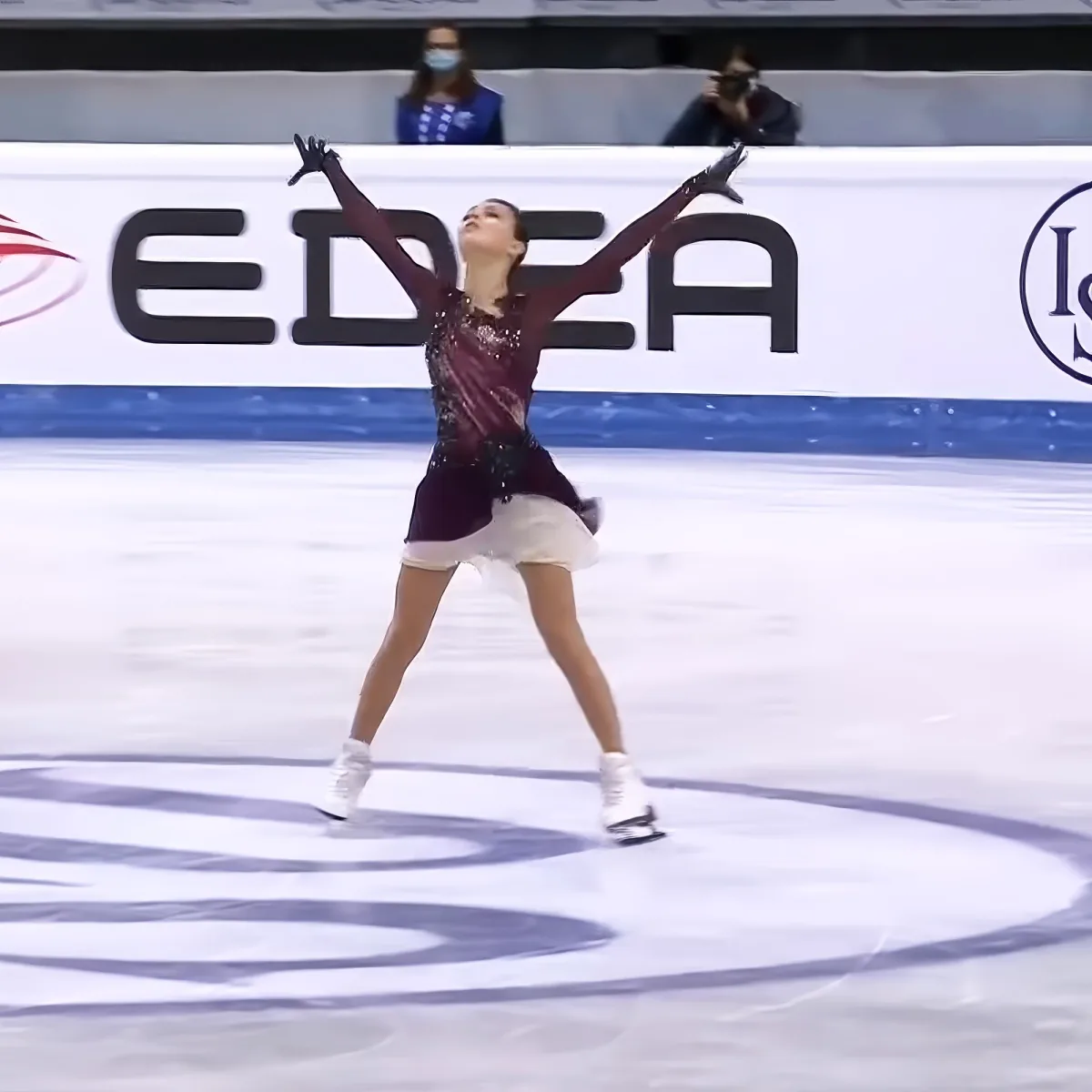 A figure skater in a maroon and white outfit performs a pose on the ice.