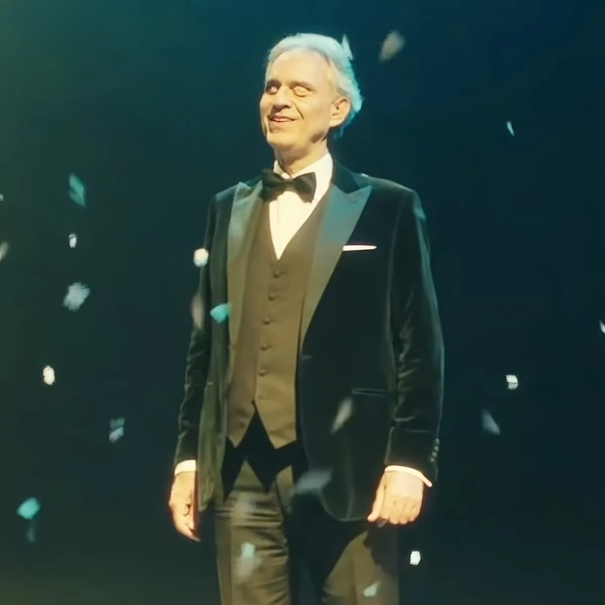 A man in a tuxedo smiles on stage with confetti falling around him.