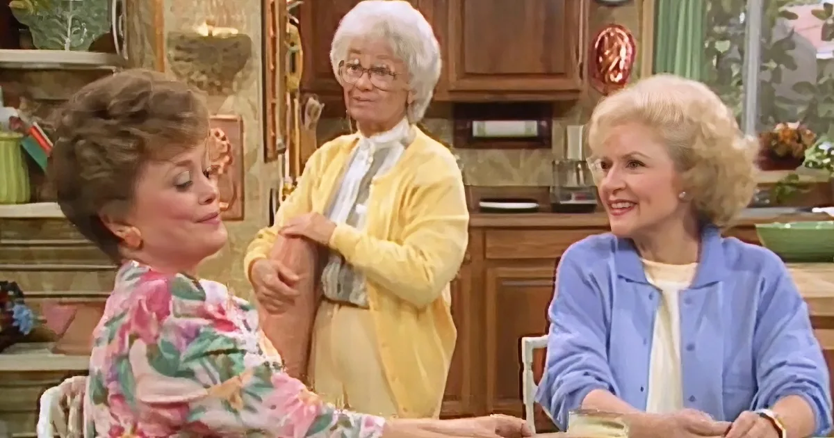 A woman in a floral shirt is sitting at a table, holding hands with another woman in a yellow cardigan, while a third...