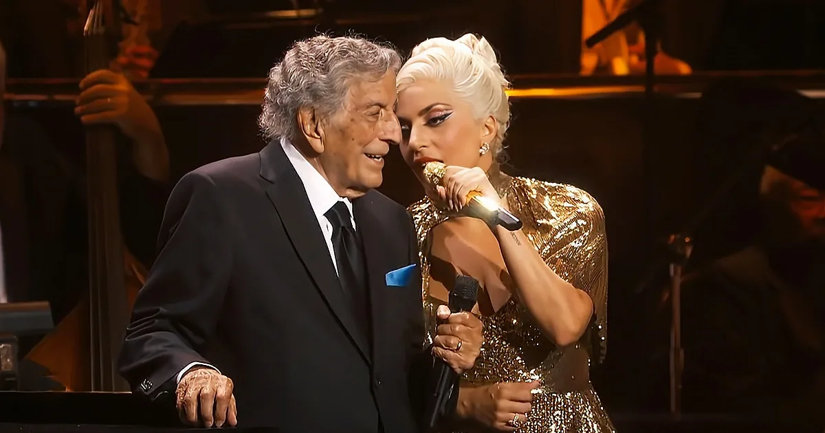 Tony Bennett and Lady Gaga share a moment on stage, both holding microphones.