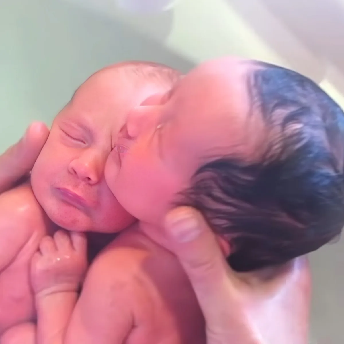 Two newborn babies are being held and bathed, appearing peaceful and serene.