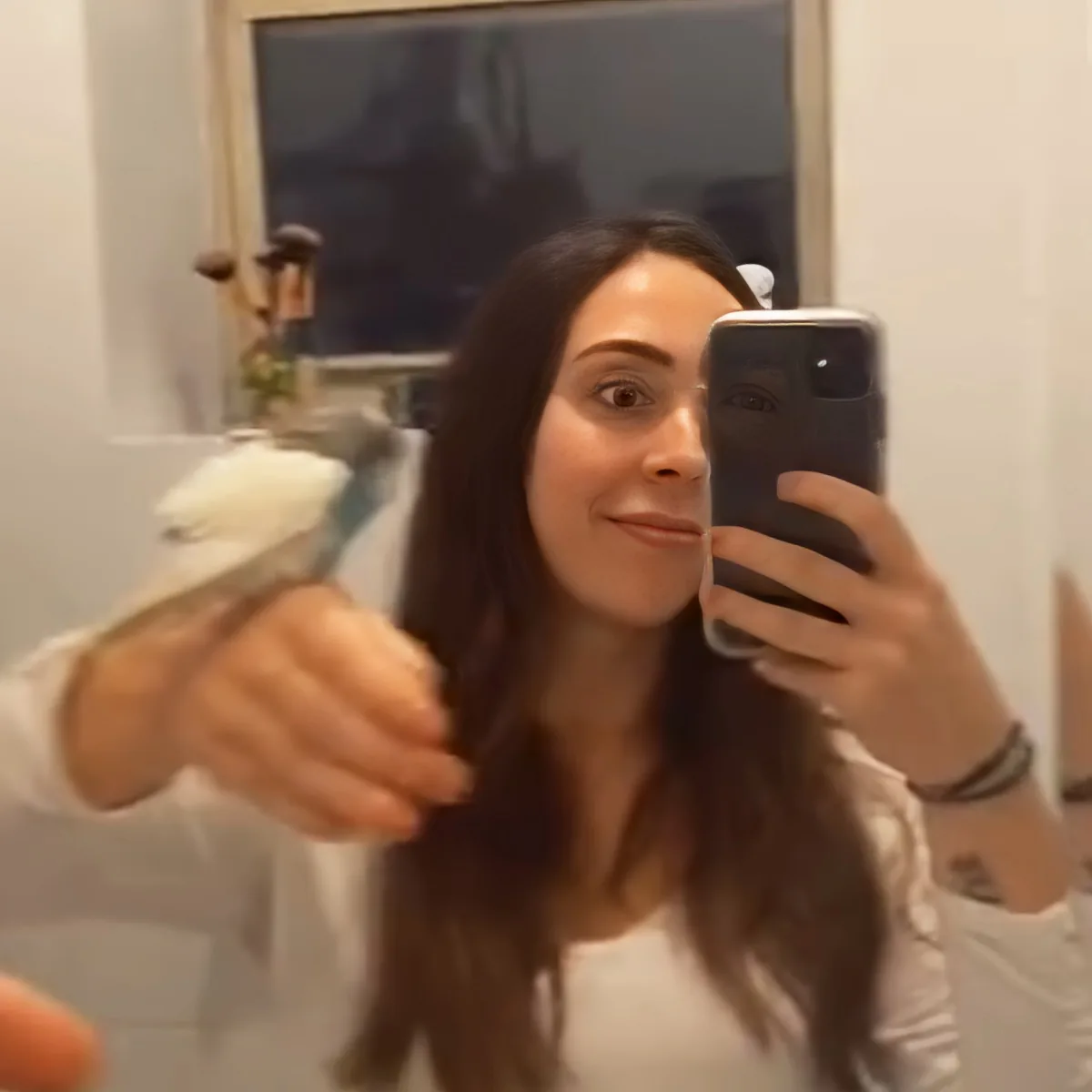 A person is taking a selfie in a mirror while brushing their hair with a white brush.