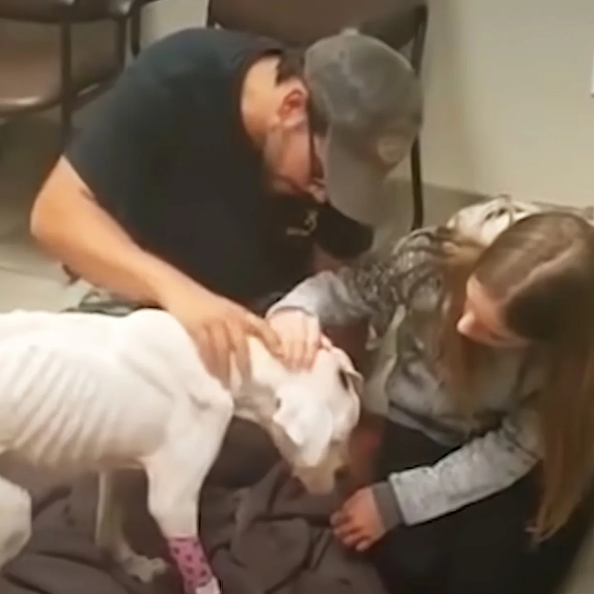 A person in a black hoodie and cap is playfully interacting with two children on the floor.