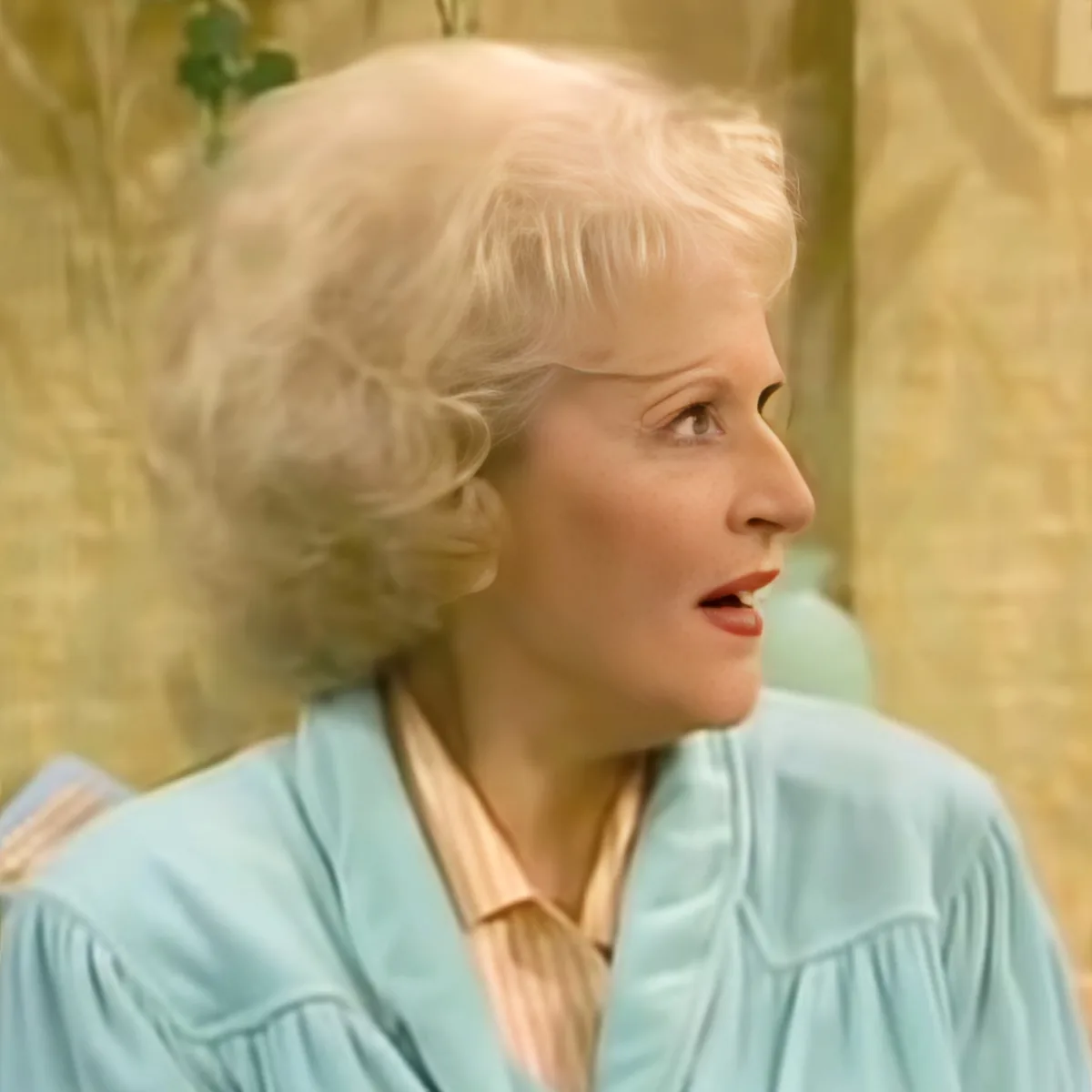A person with light-colored hair, wearing a light blue top, is looking to the side with a thoughtful expression.