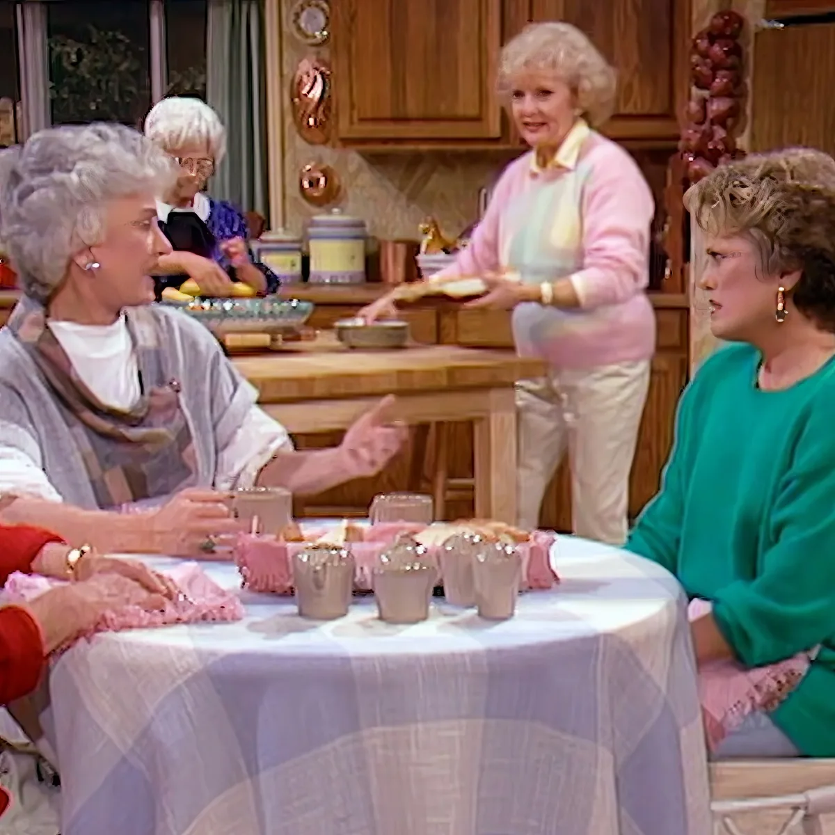A woman in a pink sweater serves food to another woman at a table with a white tablecloth.