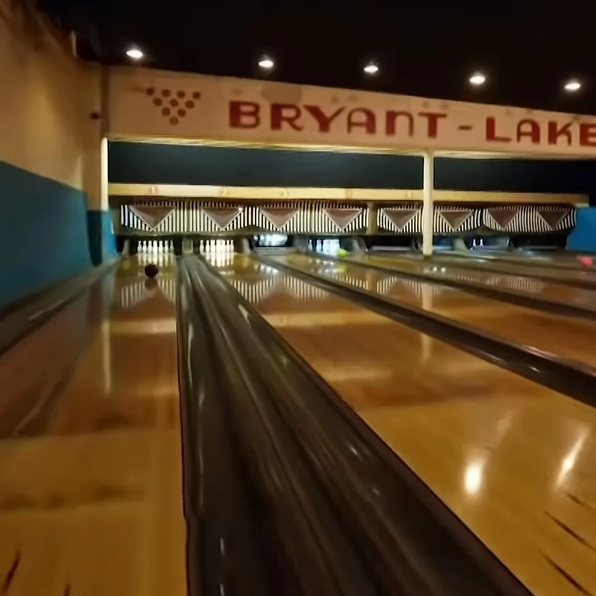 A bowling ball rolls down a lane at Bryant Lake bowling alley, with pins and a sign above.