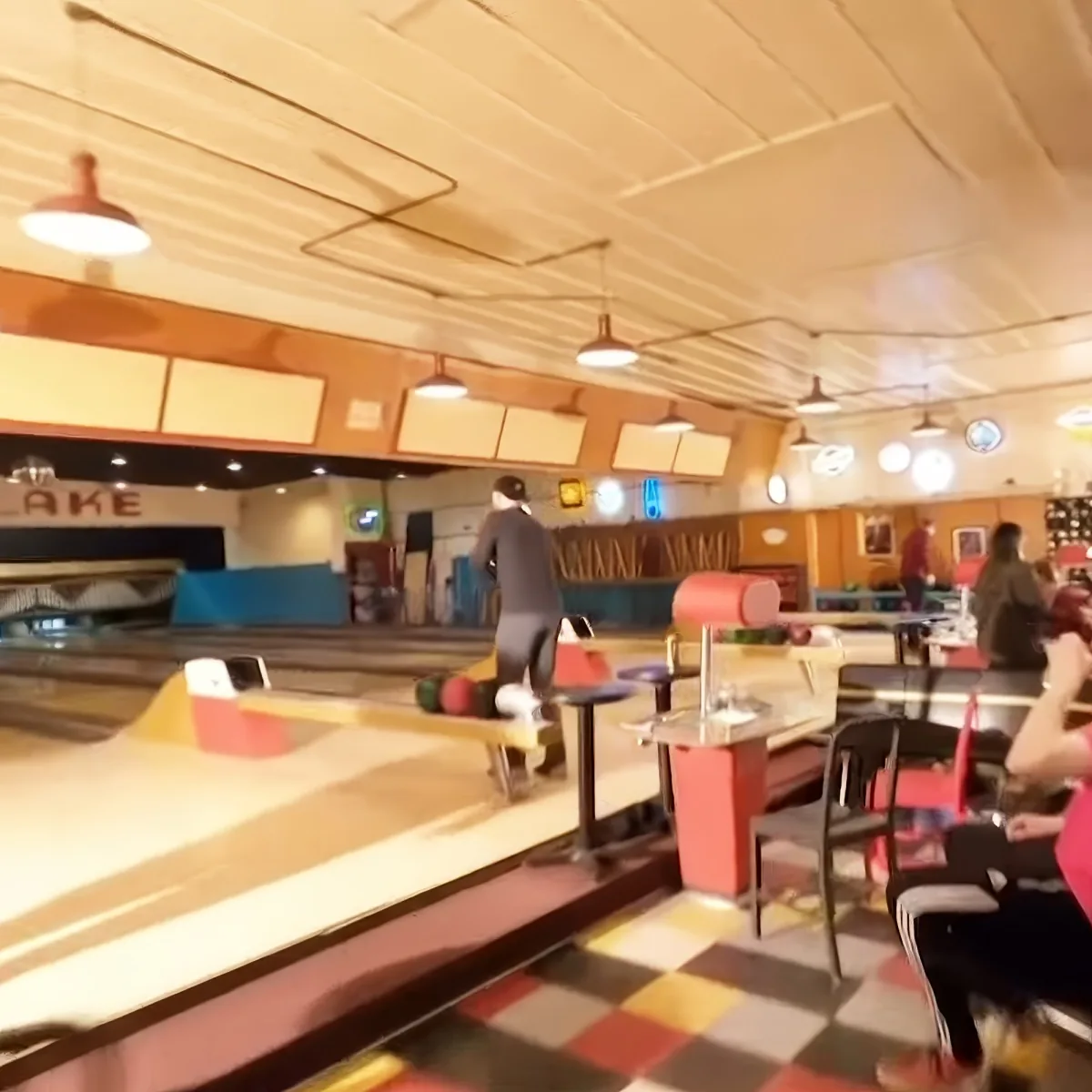 A person in a black outfit stands at a bowling lane, preparing to bowl.