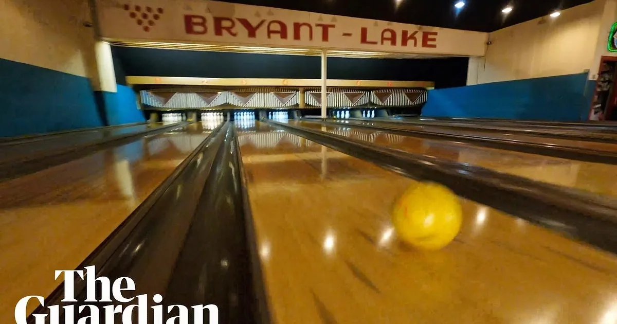 A yellow bowling ball rolls down a polished lane towards the pins.