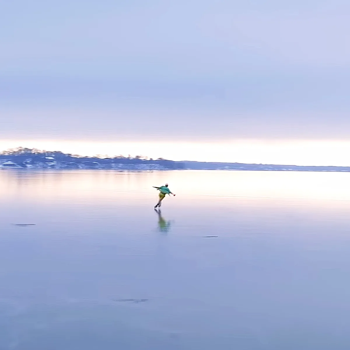 A person in a green jacket skates on a frozen lake under a clear sky.