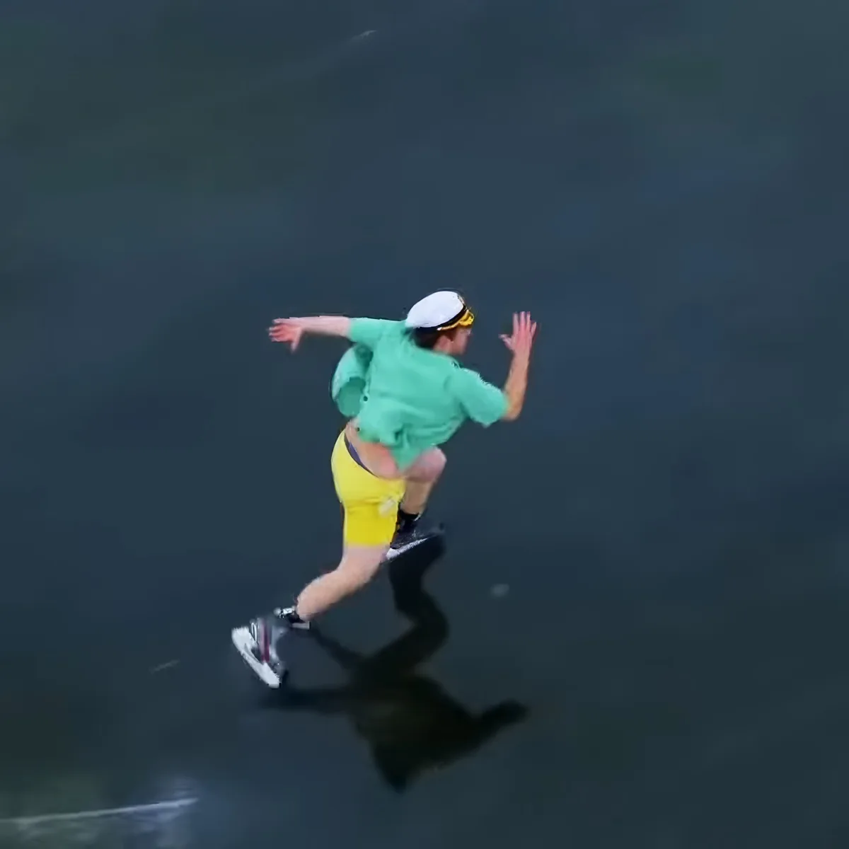 A person in a green shirt and yellow shorts is wakeboarding on dark water.