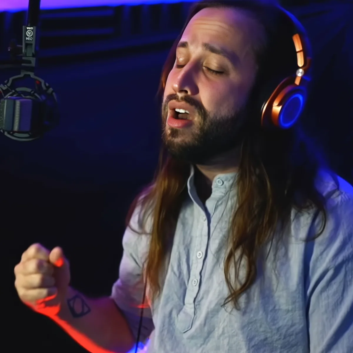 A man with long hair and beard, wearing headphones, sings passionately in a dimly lit studio.