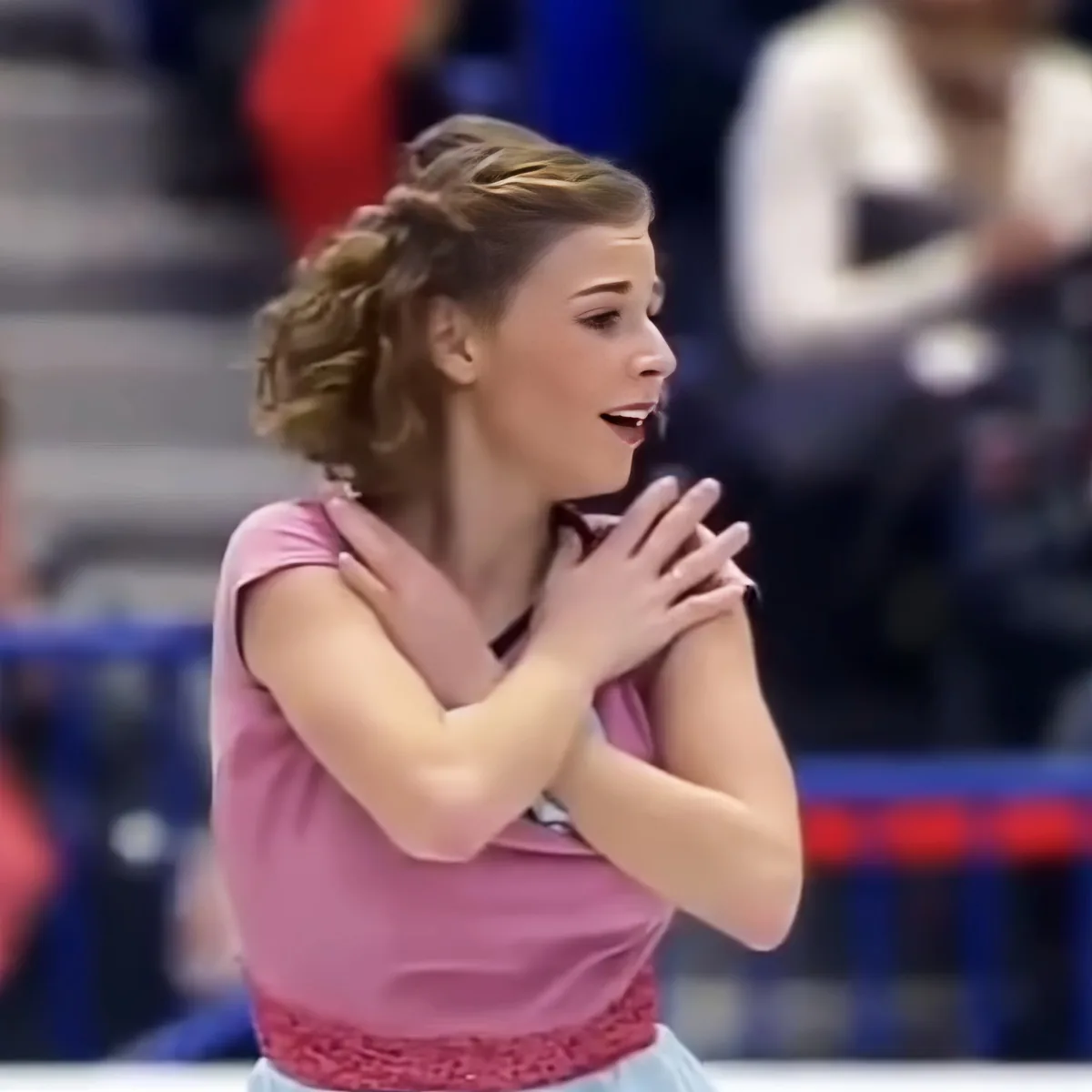 A woman in a pink outfit with her hands clasped together, possibly in a moment of reflection or emotion.