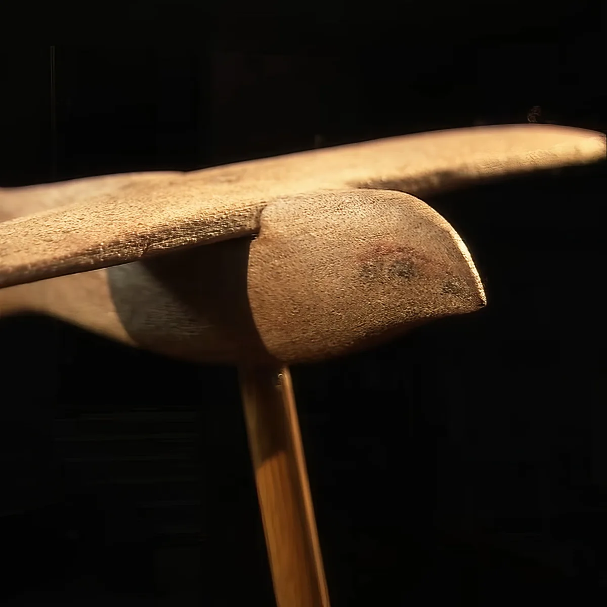 A close-up of a wooden chair with a curved backrest and a dark background.