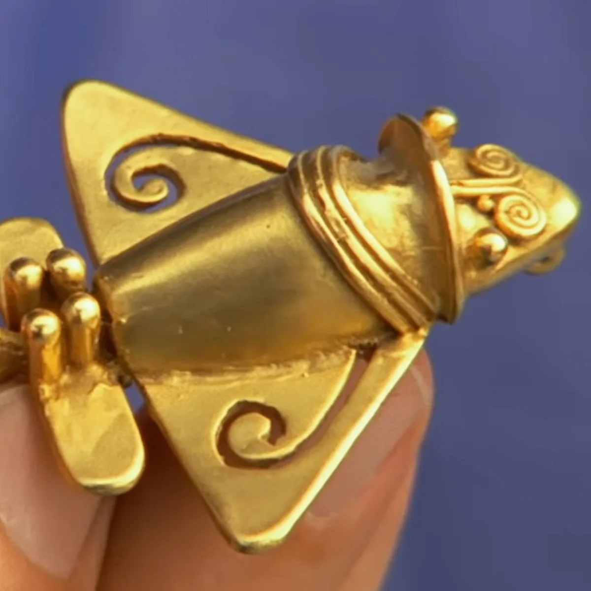 A golden frog figurine with intricate details and a crown is being held.
