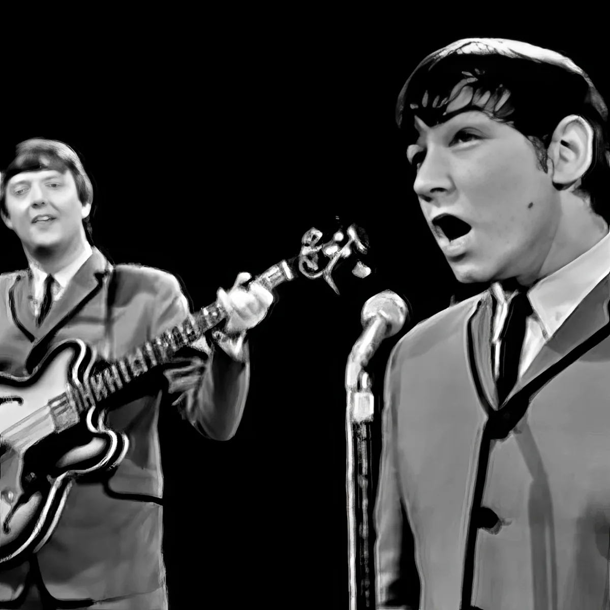 A man sings into a microphone while another plays guitar on stage.