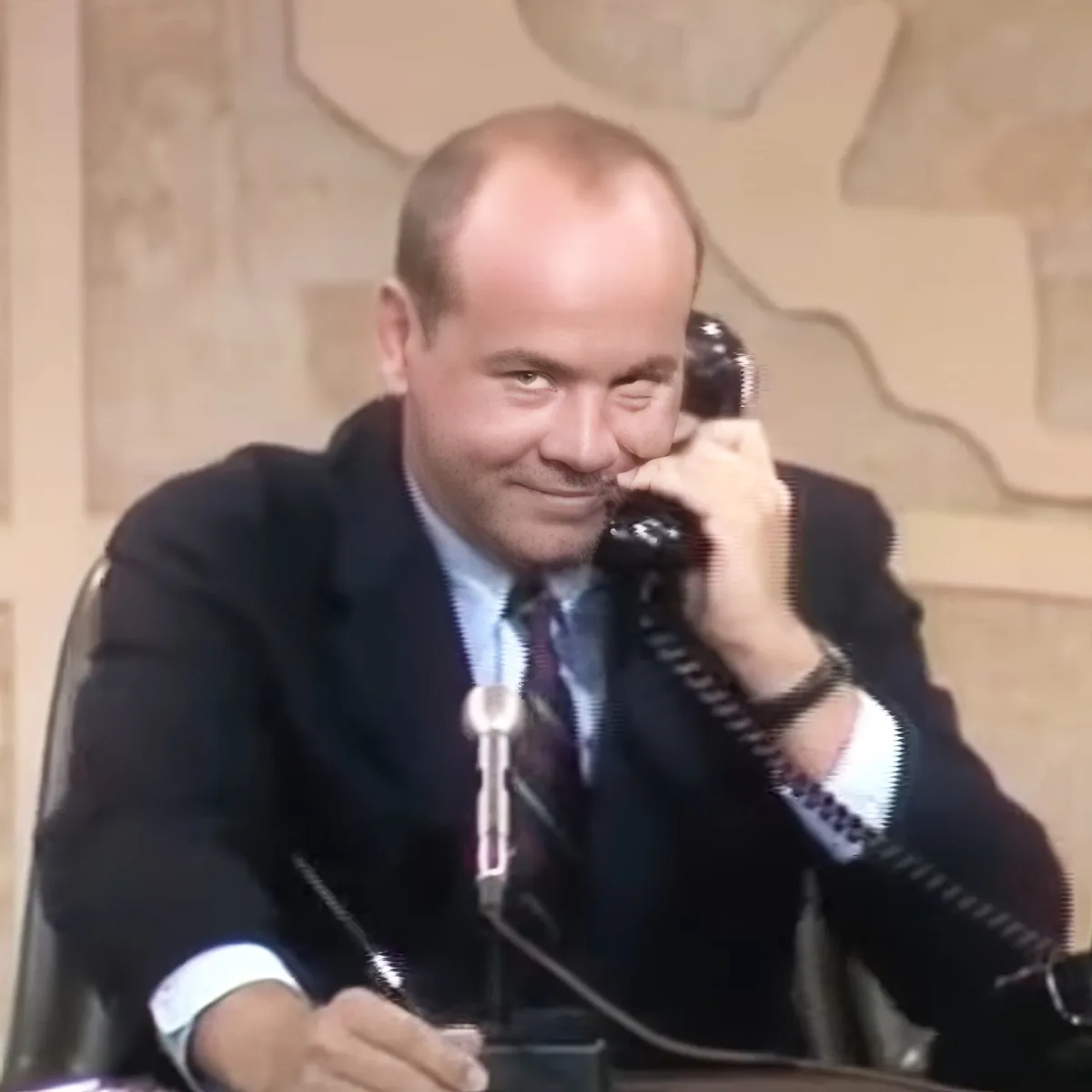 A man in a suit and tie is smiling while holding a telephone to his ear.