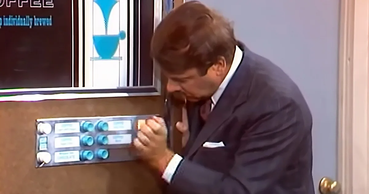 A man in a suit is pressing buttons on a coffee machine, appearing focused.