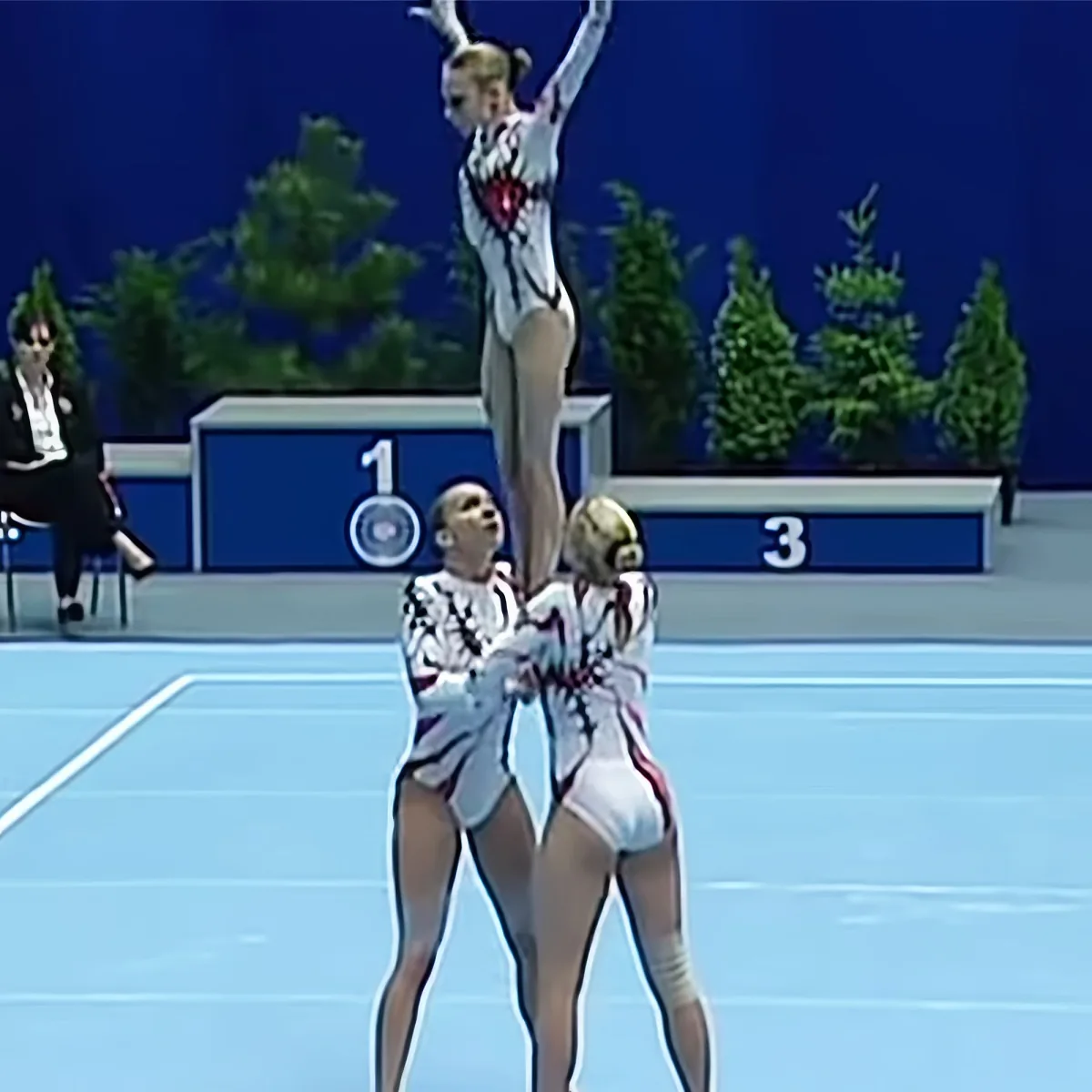 Three gymnasts perform a synchronized routine on a blue floor, showcasing their skills and teamwork.