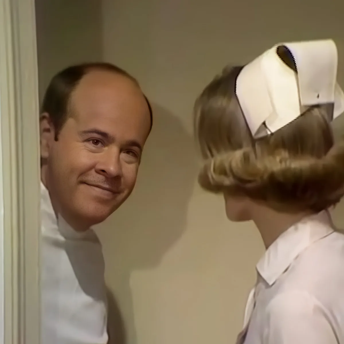 A man in a white shirt smiles at a woman in a nurse's uniform with a white cap.