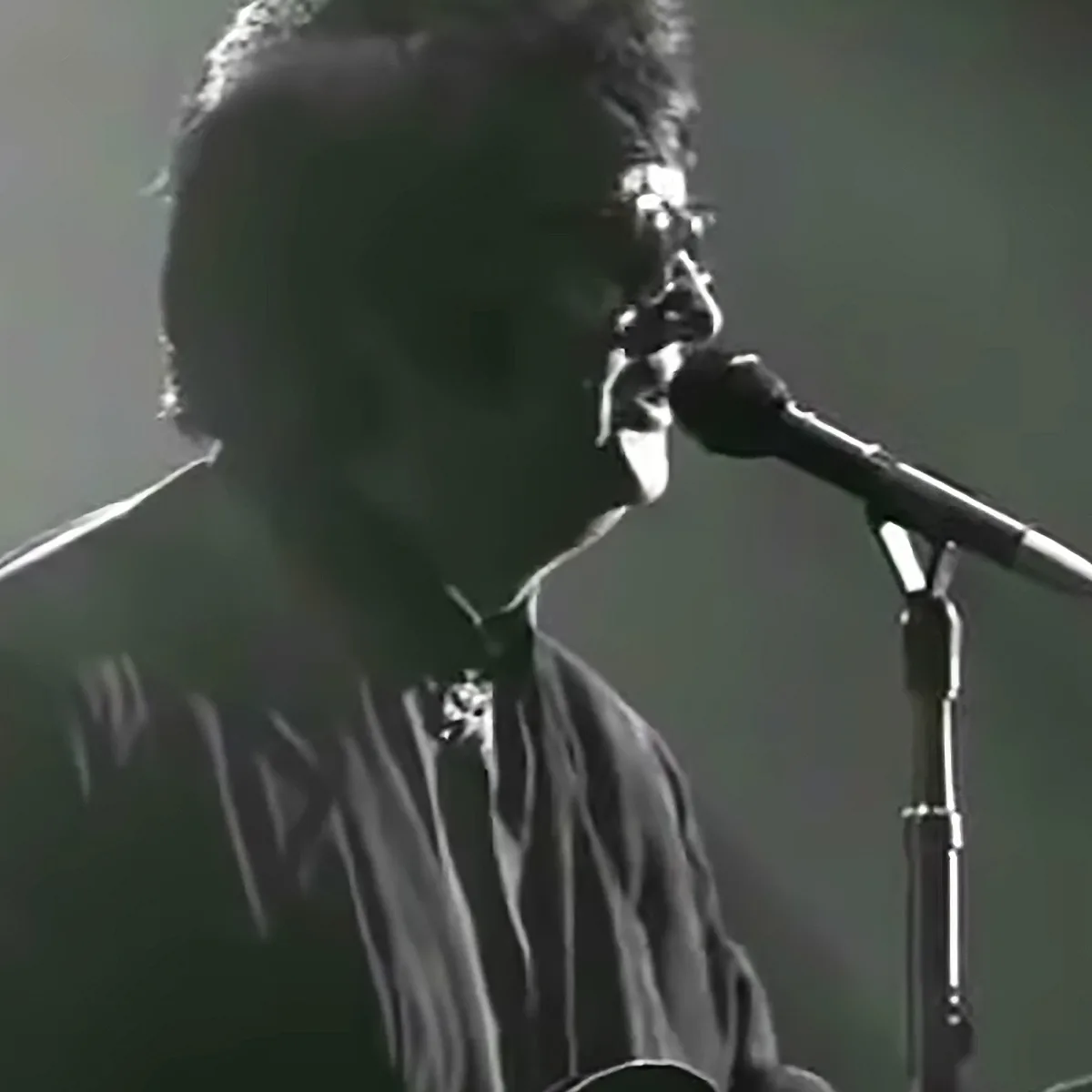 A person wearing glasses and a striped shirt sings into a microphone.