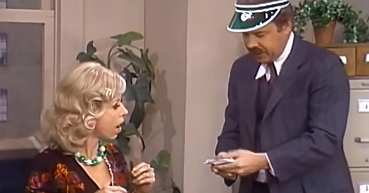 A woman with blonde hair and a man in a uniform are interacting, with the man holding papers.