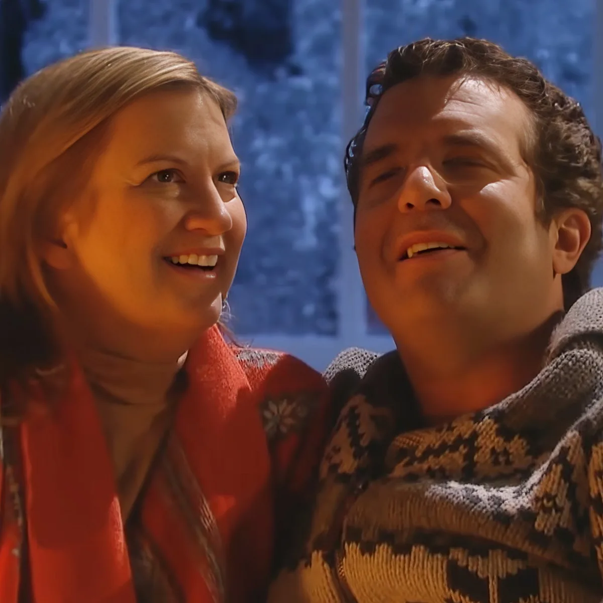 A man and woman, both smiling, are wrapped in a cozy blanket, suggesting a warm, intimate moment.