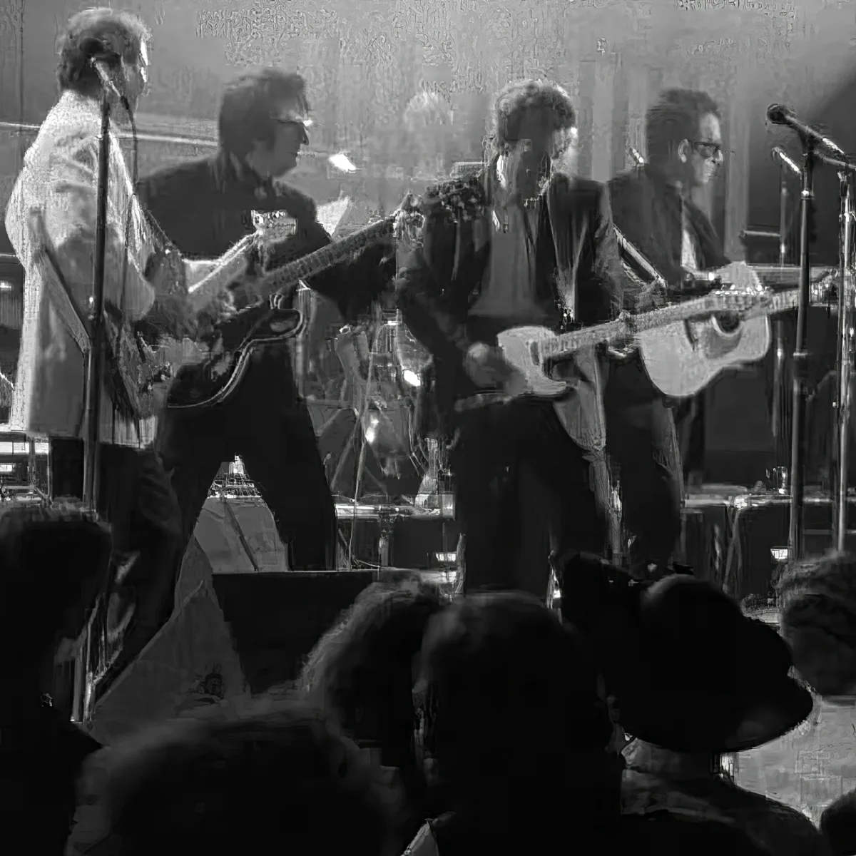 A band performs on stage, with guitarists and a drummer, in front of an audience.