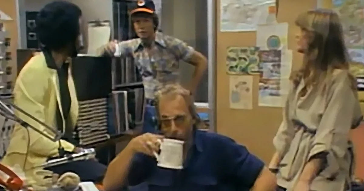 A man in a blue shirt drinks from a cup while others interact in the background.