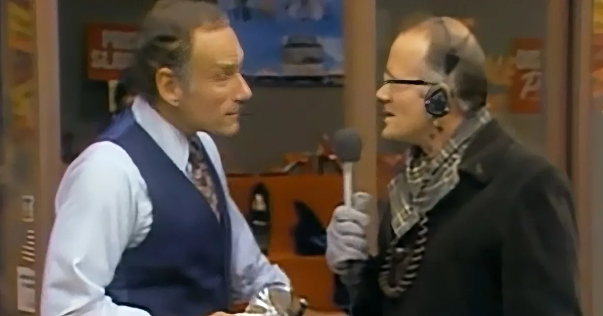 A man in a vest and tie is being interviewed by a woman holding a microphone.
