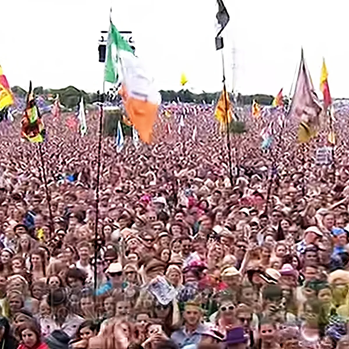 A massive crowd of people at a festival with colorful flags flying overhead.